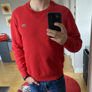 Röd Lacoste tröja - En magisk tröja till alla säsonger. Modellen i bilden är 177Cm. Tröjan är i som i nyskick och har bara använts ett fåtal gånger. Storleken på tröjan är S men passar även M. Original priset på tröjan är 1445kr men säljer min för bara 449kr.