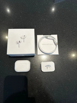 Apple AirPods Pro med laddningsetui - Säljer ett par vita Apple AirPods Pro med trådlöst laddningsetui. Hörlurarna har in-ear-design, silikonproppar och levereras med originalkartong, USB-C laddkabel och extra öronproppar. Snygg och stilren design i plast, perfekt för musik och samtal.       Hör av dig för mer information.