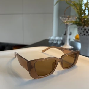 Bruna rektangulära solglasögon - Snygga solglasögon med rektangulära bågar i transparent brun. Glasen är tonade i brunt och bågarna har en modern, kantig design🤎🤎