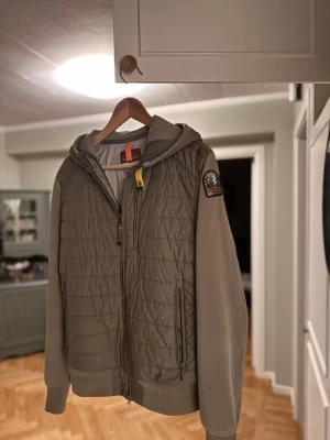 Parajumper cardigan (M) - Tjenare! Säljer denna feta olivgröna parajumper cardigan i storlek M, finns inga defekter förutom att det inte är några snören runt luvan som jag tagit bort, tycker personligen att det är fetare utan. Skriv vid frågor eller liknande! 