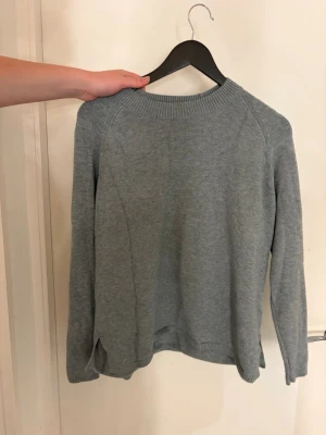 Ljusgrå stickad tröja från JDY - Mysig ljusgrå stickad tröja från JDY med rund halsringning och långa ärmar. Tröjan har en enkel och stilren design med ribbade muddar vid hals, ärmslut och nederkant. Perfekt för lager på lager under kyliga dagar.