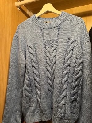 Tiger of Sweden tröja - Säljer en ljusblå kabelstickad tröja med grova flätmönster framtill och på ärmarna. Tröjan har rund halsringning och ribbade muddar vid ärmslut och nederkant. Perfekt för dig som gillar en mysig och trendig look.✨💙