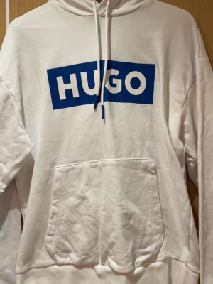 Vit hoodie från HUGO med blå logga - Snygg vit hoodie från HUGO med stor blå logga framtill. Har endast användst 1-2 gånger. Äkta