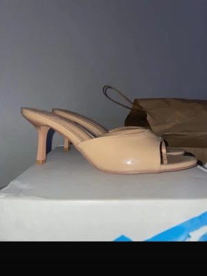 Beige lackade slip-in pumps - Snygga beige slip-in pumps med öppen tå och låg klack. Skorna har en stilren design i glansigt lackmaterial och en bekväm passform. Perfekta för att lyfta vilken outfit som helst med en chic touch.