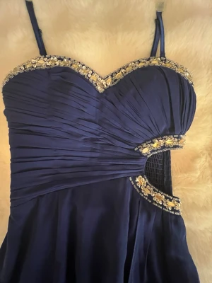 Marinblå långklänning med paljettdetaljer - Elegant marinblå långklänning med smala axelband och glittrande paljettdetaljer längs byst och midja. Klänningen har en snygg cut-out vid sidan och draperad överdel som ger en lyxig känsla. Perfekt för speciella tillfällen. Varan är i bra skick! Banden går även att tas bort💗