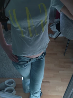 Ljusgrå croppad GAP t-shirt - Säljer en ljusgrå croppad t-shirt från GAP med stort gult tryck framtill. T-shirten har korta ärmar och en avslappnad passform. Perfekt för dig som gillar en enkel men snygg stil.