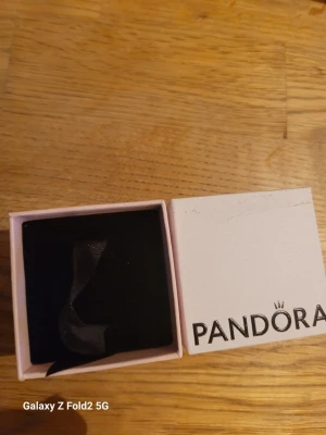 Pandora smyckesask i rosa och vitt - Säljer en snygg smyckesask från Pandora i ljusrosa och vitt. Asken har svart insida med band för att hålla smycken på plats. Perfekt för att förvara eller ge bort smycken i. Klassisk Pandora-logga på locket.