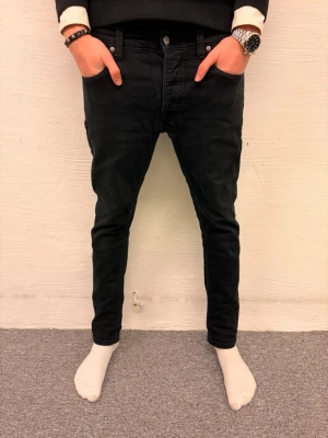 Svarta slim jeans från Nudie - Modellen är 185cm 65kg|Pris går att diskuteras|Svarta jeans från Nudie Jeans med skinny passform och klassisk femficksdesign. Jeansen har knappgylf och subtila sömdetaljer på bakfickorna. Materialet är jeans i bomull och de har en lågmidjad siluett som sitter tight längs benen.
