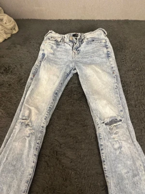Ljusblå slitna jeans från true religon  - Säljer ett par ljusblå jeans från true religon med snyggt slitna detaljer på båda benen. Storlek w27