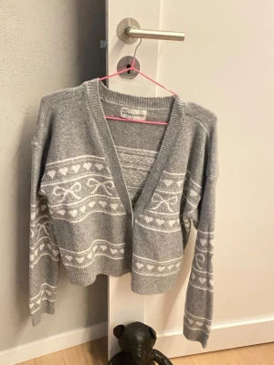stickad kofta - Mysig grå stickad kofta från No Boundaries med vita mönster i form av hjärtan och slingor. Koftan har V-ringning, ribbade muddar och är något croppad i modellen. Perfekt för lager på lager och en avslappnad stil. KÖPT PÅ WALMART I USA. 🇺🇸 