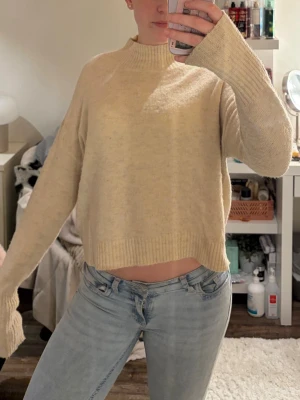 Beige stickad tröja från Bik Bok - Beige stickad tröja från Bik Bok med hög hals och avslappnad passform. Tröjan har långa ärmar och ribbstickade detaljer vid hals, ärmslut och nederkant. Perfekt för lager-på-lager och enkel att matcha med jeans eller kjol.