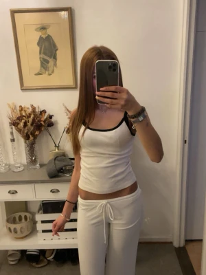 Vitt loungewear-set med svarta detaljer - Snyggt och bekvämt loungewear-set i vitt med svarta kanter. Setet består av ett linne med smala axelband och matchande byxor med dragsko i midjan. Perfekt för en avslappnad dag hemma.