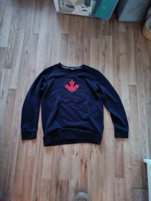 Mörkblå sweatshirt från Dsquared2 - Cool svart sweatshirt från Dsquared2 med röd lönnlöv-tryck och broderad logga på bröstet. Tröjan har rund halsringning och långa ärmar. Perfekt för dig som gillar streetwear och vill sticka ut med en snygg detalj.