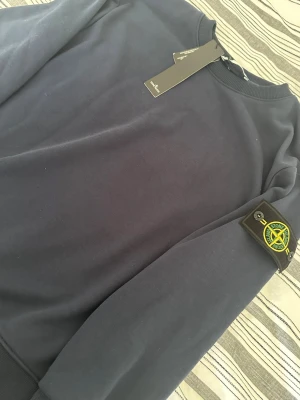 Mörkblå sweatshirt från Stone Island - Snygg mörkblå sweatshirt från Stone Island med klassisk rund hals och ikonisk logotyp-patch på vänster ärm. Tröjan har en enkel och stilren design. Tillverkad i mjukt bomullsmaterial för extra komfort.