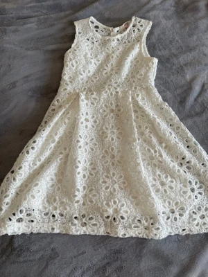 Vit spetsklänning från Redtag - Söt vit klänning från Redtag med blommig spets och rund halsringning. Klänningen är ärmlös och har en fin, utsvängd kjol samt dragkedja i ryggen. Perfekt för sommarens alla tillfällen!