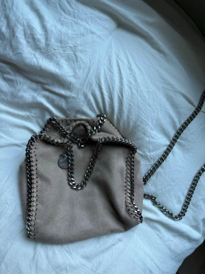  Stella McCartney handväska -  beige handväska från Stella McCartney med kedjedetaljer i silver runt kanterna och som axelband.  Modellen är tiny falabella!