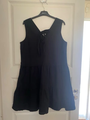 Svart ärmlös linnéklänning med knyt - Svart kortklänning i linne med ärmlös design och v-ringad rygg. Klänningen har ett knytband i ryggen och en loose passform som ger en avslappnad look. Perfekt för sommardagar och enkel att matcha med olika accessoarer. Kolla gärna mina andra annonser❗️