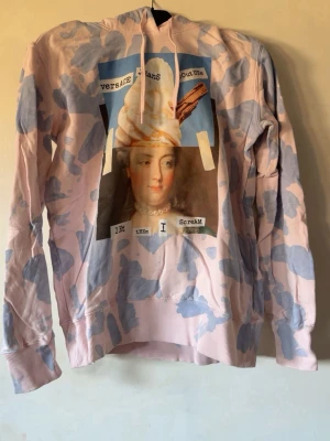 Pastellrosa hoodie Versace Jeans hoodie  - Unik hoodie från Versace Jeans Couture i pastellrosa med blått camo-mönster. Stor tryckt bild med glass och text på bröstet. Hoodien har huva med dragsko och ribbade muddar. Perfekt för dig som vill sticka ut med streetwear-vibe.