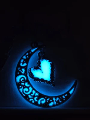 Glow in the dark mån- och hjärthalsband - Unikt handgjort halsband i silverfärgad metall med en halvmåne dekorerad med snirkliga mönster och ett hjärthänge som lyser i mörkret efter att ha absorberat dagsljus utifrån eller solljus, en kort stund. Kedjan har justerbar längd och är gjort av rostfritt stål. Perfekt för dig som gillar magiska detaljer och statement-smycken. Hänget är ca 3 cm och kedjan 50 cm.