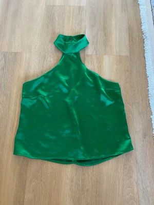 Grön halterneck topp från Gina Tricot - Snygg grön halterneck topp från Gina Tricot i glansigt satinliknande material. Toppen har hög krage och är ärmlös med en stilren, croppad passform. Perfekt för dig som vill sticka ut med en färgstark look.
