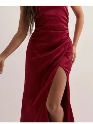 Vinröd långklänning från Nelly - Vinröd långklänning från Nelly med elegant slits framtill. Klänningen har figurnära passform och är perfekt för dig som vill sticka ut. Tillverkad i ett mjukt polyestertyg som känns bekvämt mot huden.