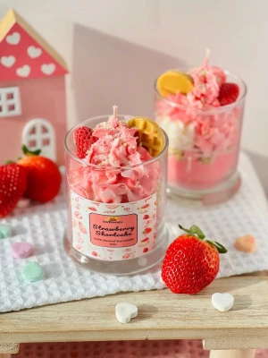 Strawberry Shortcake doftljus i glas - Unikt doftljus i glas som ser ut som en jordgubbstårta med rosa och vit topping, dekorerat med en konstgjord jordgubbe och liten kexbit. Ljuset har en söt etikett och är perfekt som dekoration eller present.  