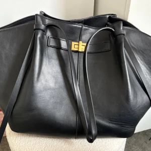 Gina tricot Long strap pu bag  - Trendig svart väska från Gina tricot, Long strap pu bag med dragsko och guldfärgat spänne framtill. Väskan har en rymlig form och minimalistisk design, Långa axelband och magnetknäppning upptill. (Det ena axelbandets typ har lossat lite)