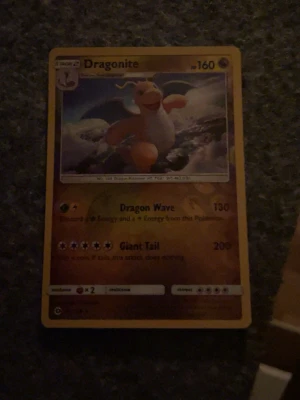 Dragonite Pokémonkort - Dragonite Pokémonkort med gul ram och färgstark illustration av Dragonite som flyger bland moln. Kortet har attackerna Dragon Wave och Giant Tail samt HP 160. Baksidan har klassiskt blått Pokémon-motiv med Pokéboll.