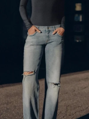 Ljusblå raka jeans med slitningar - Säljer ett par ljusblå jeans med raka ben och snygga slitningar vid knäna. Jeansen har klassisk femficksdesign och hög midja. Perfekta för en avslappnad och trendig look. Har lite missfärgningar 