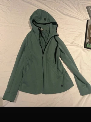 Grön hoodie från Sail Racing - Snygg grön hoodie från Sail Racing med dragkedja framtill och svarta detaljer vid huvan. Tillverkad i mjukt material och har två fickor på sidorna. Perfekt för dig som gillar en clean och sportig stil. Den är även använd max 10 gånger och ligger i en låda ett tag. 