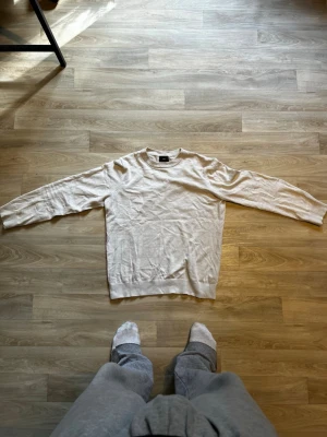 Vit basic tröja med rund hals - En enkel och stilren vit tröja med rund halsringning och långa ärmar. Tröjan har en rak passform och ribbade muddar vid ärmslut och nederkant. Perfekt att matcha med jeans eller över en skjorta för en clean look.