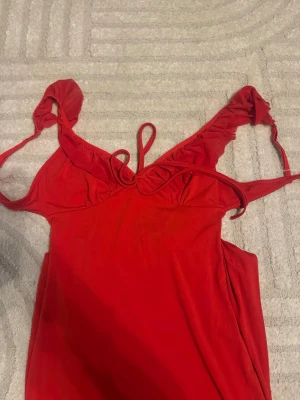 Röd ärmlös klänning med knytband - En röd klänning med tunna axelband som knyts och v-ringad urringning. Tillverkat i ett mjukt och följsamt material som känns skönt mot huden. Perfekt för avslappnade kvällar och nätter. Köpt för 200kr