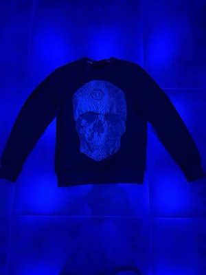 Philip plein sweatshirt - Cool svart sweatshirt med stort döskalletryck framtill. Tröjan har rund halsringning och långa ärmar. Perfekt för dig som gillar streetwear och vill sticka ut med en edgy look. Materialet känns mjukt och bekvämt mot huden.