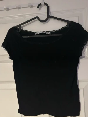 Topp med spets  - Säljer en svart croppad topp med korta ärmar och söt spetskant vid halsringningen och ärmsluten. Toppenär perfekt för dig som gillar en enkel men ändå snygg stil.(ifrån lager 157)