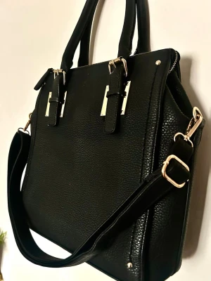 Minimalistisk svart Tote / Jobbväska – Perfekt för skola/jobb! - Köpt på Accent. Det bästa med denna är att den är helt utan synliga loggor på utsidan – väldigt ”clean girl aesthetic” och lätt att matcha till allt! 🖤 Superfin & stilren väska i strukturerad läderimitation från Accent. Helt utan synliga loggor för en lyxig ”clean girl aesthetic”! 🖤 Rymlig modell som passar perfekt för laptop eller mappar. • Mått: 40x33 cm • Guldfärgade detaljer & justerbara handtag • Avtagbar axelrem ingår! • Nyskick