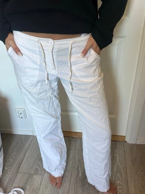 Vita linnebyxor  - Säljer ett par vita linnebyxor med raka ben och dragsko i midjan. Byxorna har två stora fickor fram och stängs med knapp och dragkedja. Perfekta för en avslappnad och stilren look. Materialet är lätt och luftigt linne.
