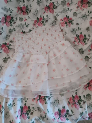 Vit blommig kjol - Supersöt kortkjol i vitt med små rosa blommor och volangdetaljer.🌸🩷 Gjord i ett lätt o luftigt material som känns perfekt för varmare dagar. 30 kr + frakt☺️