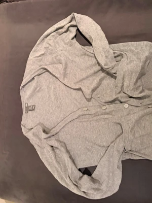 Grå kofta från H&M med knappar - Säljer en tunn, grå kofta från H&M i storlek S. Koftan har långa ärmar, rund halsringning och stängs med flera knappar framtill. Tillverkad i mjukt och stretchigt material som passar perfekt till lager på lager-stil.