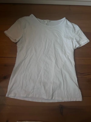 Vit basic t-shirt från H&M - Klassisk vit t-shirt från H&M med rund hals och korta ärmar. Tillverkad i mjuk bomull som känns skön mot huden. Enkel och stilren modell som funkar till det mesta och är ett måste i garderoben.