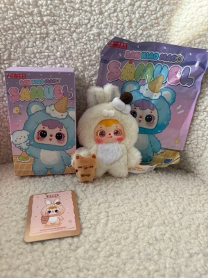 Samlingsfigur Sam Xiao Mao Samuel - Söt samlingsfigur från Sam Xiao Mao-serien, modell Samuel. Dockan har ett mjukt vitt plyschdjurdräkt med kaninöron och bruna detaljer samt ett litet gosedjur. Kommer med originalförpackning och samlarkort.