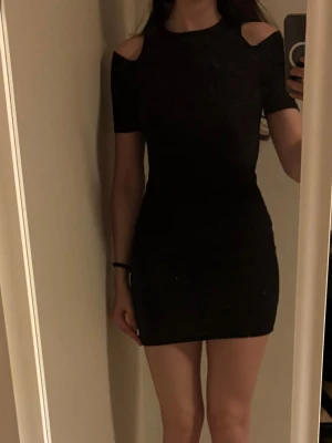 Svart kort klänning med cut out - Snygg svart kort klänning med cut out-detaljer vid axlarna och tight passform. Klänningen har korta ärmar. 