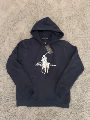 Mörkblå hoodie från Polo Ralph Lauren - Säljer en skit snygg mörkblå Ralph lauren hoodie! Tröjan är i storlek M men är slim model så passar storlek S lite bättre. Tröjan är helt ny, oanvänd, bara testad🤙. Tröjan kommer även med prislapp och påse. Priset är ej hugget i sten så kom gärna med bud!