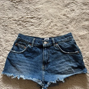 Blå jeansshorts urban outfitters - Snygga blå jeansshorts från BDC med fransig rå kant och klassisk femficksdesign. Shortsen har bälteshällor och knappstängning framtill. Perfekta för varma dagar och en avslappnad stil.