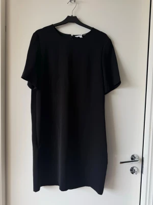 Svart klänning från & Other Stories - En stilren svart klänning från & Other Stories med rund halsringning och korta ärmar. Klänningen har en rak passform och stängs med dragkedja i ryggen. Perfekt för dig som gillar minimalistisk och tidlös design. Har fickor 