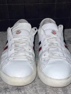 Vita Moncler sneakers med ränder - Snygga vita sneakers från Moncler med klassiska röda och marinblå ränder på sidan och Moncler-logga. 