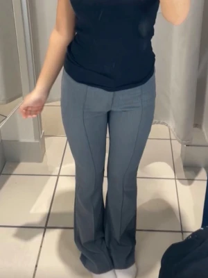 Grå bootcut kostymbyxor - Snygga grå kostymbyxor med klassiska pressveck och bootcut-modell. Byxorna har en figurnära passform upptill och släpper ut vid benen. Perfekta för dig som vill ha en stilren och modern look. Materialet är mjukt och följsamt.