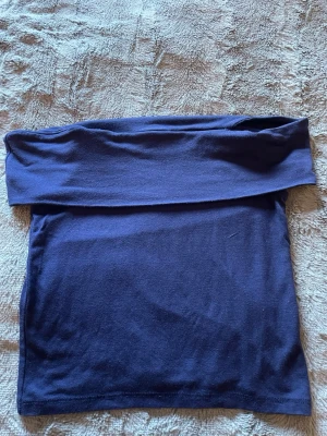 Marinblå ofshoulder topp - Snygg marinblå tubtopp från Kappahl i mjukt bomullsmaterial. Enkel och stilren design utan mönster eller detaljer, perfekt att matcha med olika outfits. Toppen är axelbandslös och har en klassisk bandeauform.