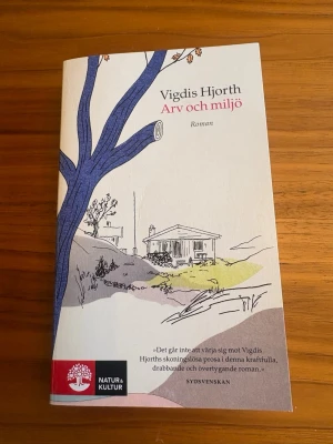 Arv och miljö av Vigdis Hjorth - Romanen 'Arv och miljö' av Vigdis Hjorth är en pocketbok med ett omslag i ljusa färger och illustration av ett hus och ett träd. Boken utforskar familjerelationer, arv och hemligheter. Utgiven av Natur & Kultur.