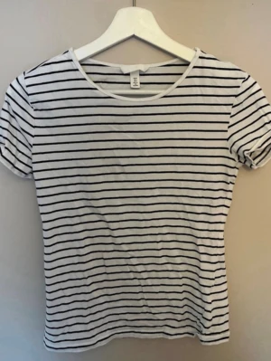 Randig t-shirt från H&M - Vit t-shirt med svarta horisontella ränder från H&M. Klassisk rund halsringning och korta ärmar. Perfekt för en avslappnad och stilren look. Tillverkad i mjukt och bekvämt material.