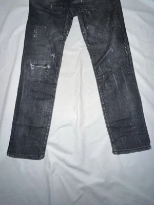 Grå jeans med slitna detaljer - Säljer ett par grå jeans med coola slitna detaljer och vita färgstänk. Jeansen har raka ben och klassiska fickor både fram och bak. Materialet är denim och de har en trendig, lite vintage look.